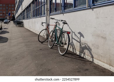 Sunny view of two bicycle lean against wall outside the building on the sidewalk beside the street in Copenhagen. 