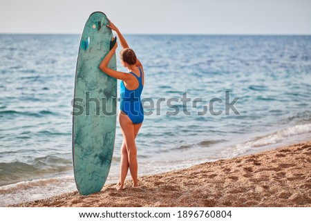 Sunny weather on beach, woman with surfboard. Calm sea, sandy coastline. Summer vacation and adventure idea. Copy space