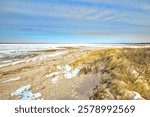 Sunny Winter day landscape of a sandy beach beside long yellow grasses and patches of snow at Skaket Beach on Cape Cod, near Orleans, Massachusetts.