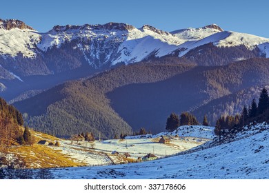 Sunny winter morning landscape with Bucegi mountains range and scattered ancient houses or farms in the valley, Fundata village, Brasov county, Romania.