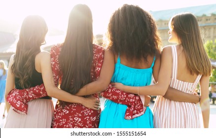 Sunny Women Days. A Group Of Four Best Friends In Magnificent Summer Outfits Are Hugging Each Other And Posing With Their Backs To The Camera.