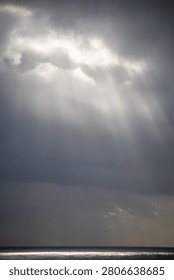 Sunrays pierce through thick clouds over a calm ocean.