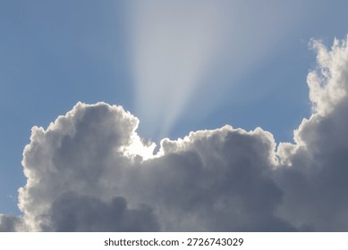 Sunrays piercing through dark clouds against a bright blue sky, creating a hopeful atmosphere