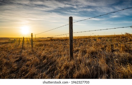 Sunrise behind a wooden barbed wire fence over natural prairie grasslands in Alberta Canada. - Shutterstock ID 1962327703
