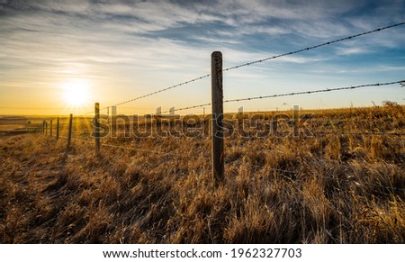 Sunrise behind a wooden barbed wire fence over natural prairie grasslands in Alberta Canada.