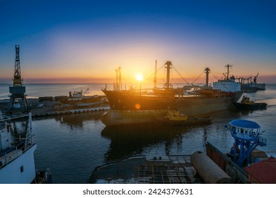 Sunrise bustling sea port, cargo ships docked at berth, cranes poised for unloading. Logistics hub for global trade, freighters ready international delivery. Early morning industrial marine terminal.