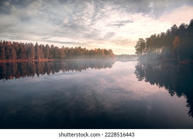 Sunrise by forest lake an early fall morning in swden with light mist over the lake, with the trees and sky relflecting in the calm water surface - Powered by Shutterstock