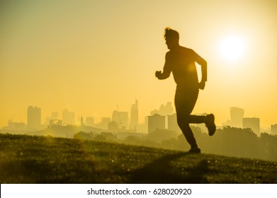 Sunrise Defocused Silhouette Of A Man Running In Front Of The City Skyline On A Hill In London, England. Focus On Building In The Background.