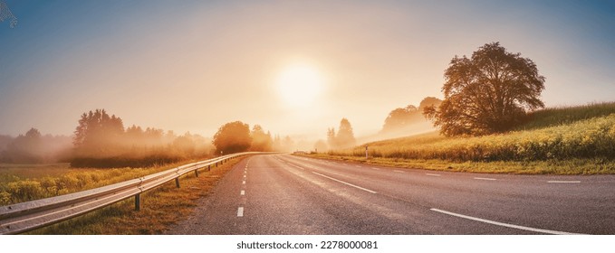Sunrise in the foggy morning on the empty asphalt country winding road.