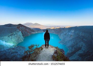 At sunrise girl stand on rock under volcano Kawah Ijen crater. Look at largest in world acid lake, sulphur mine. Popular travel destination, adventure hike on family vacation in Bali, Java, Indonesia - Powered by Shutterstock