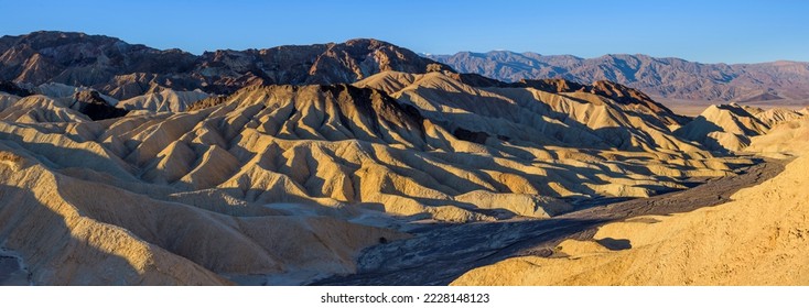 Sunrise at Golden Desert Valley - Panoramic overview of soft morning sunlight shining on colorful rolling mudstone hills, gullies and dry river bed at Zabriskie Point, Death Valley National Park, CA. - Powered by Shutterstock