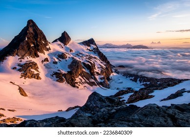 Sunrise Illuminates an Ocean of Clouds and Snowfield Peak as Two Small Climbers Ascend the Glacier Below. North Cascades National Park, Washington