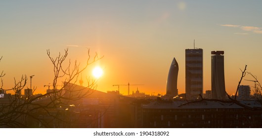 Sunrise in Milan (Italy) in backlight, with lens flares and perfect blue sky. Silhouette of towers of Citylife district in the background.
