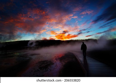 Sunrise near Yellowstone geysers with steam and silhouette of person on boardwalk