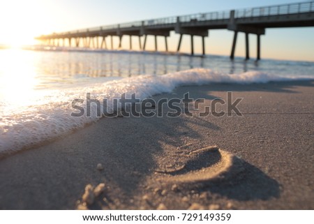 Sunrise on beach showing sand and sea foam with Jacksonville Beach Pier in background.