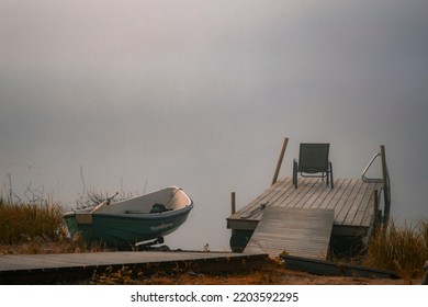 Sunrise On A Foggy Lake. Wooden Dock And A Green Boat.