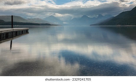 Sunrise on Lake McDonald in Glacier National Park in Montana.  Strong sky reflection on the still water.  Empty dock extending into the lake.