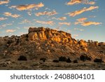 Sunrise on a Rocky Mesa in the New Mexico landscape with small puffy clouds in the blue sky.