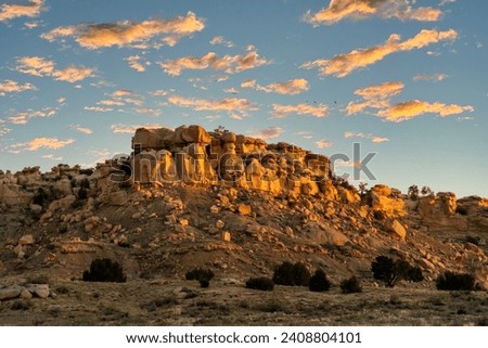 Sunrise on a Rocky Mesa in the New Mexico landscape with small puffy clouds in the blue sky.