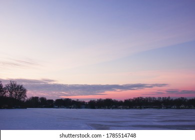 Sunrise over a cold and frozen lake. Pink, yellow, orange, and blue tones cover the sky - Powered by Shutterstock