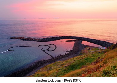 Sunrise over the Double-Heart Stacked Stones or Twin-Heart Fish Trap, which is a fishing weir and a popular tourist attraction in Cimei, Penghu, Taiwan, with golden sunlight reflected on the seawater
