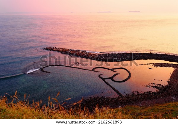 Sunrise over the Double-Heart Stacked Stones or\
Twin-Heart Fish Trap, which is a fishing weir and a popular tourist\
attraction in Cimei, Penghu, Taiwan, with golden sunlight reflected\
in the seawater