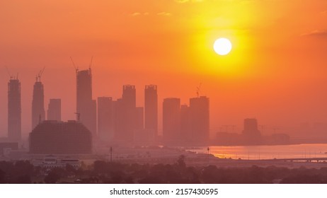 Sunrise Over Dubai Creek Harbor With Skyscrapers And Towers Under Construction Aerial Timelapse. Big Red Sun Rise Up Behind Buildings