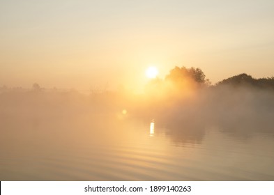 Sunrise Over The Foggy Lake With The Reflection Of Sun And Trees In The Water. Early Fresh Morning Landscape. Mist On The Water, Forest Silhouettes And The Rays Of The Rising Sun.