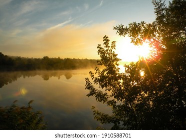 Sunrise over the foggy lake with the reflection of sun and trees in the water. Early fresh morning landscape. Mist on the water, forest silhouettes and the rays of the rising sun. - Powered by Shutterstock