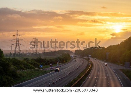 Sunrise over the M56 motorway at Frodsham, England, UK, with light traffic, roadworks and a row of pilons. Concept of early start, commute, power, industry, workers, back to work, daily grind