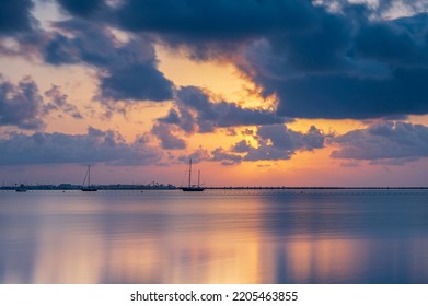 Sunrise over the Mediterranean sea, on a cloudy summers morning.  The sun is reflecting on the calm sea, on which there are a few sailing boats - Powered by Shutterstock