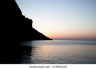 Sunrise over mountain rock in sea water. Sunrise seascape in calm sea. Rocks silhouette and golden reflections on the rippled water