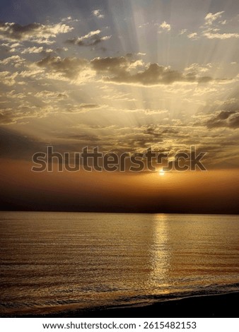 Sunrise over the sea with dramatic clouds and golden sunlight reflecting on the water. Peaceful seascape with warm tones and a tranquil morning atmosphere.