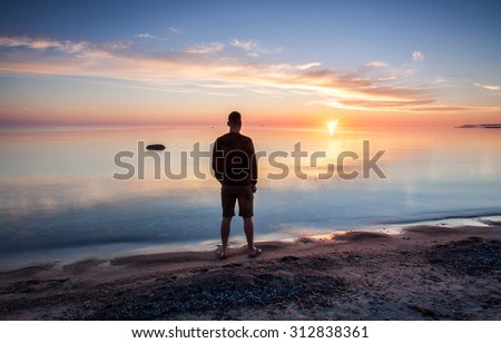 Sunrise over the sea horizon. The calm Baltic Sea is colored in blue, orange and yellow. Silhouette of a man looking at the spectacle. The island of Gotland, Sweden.