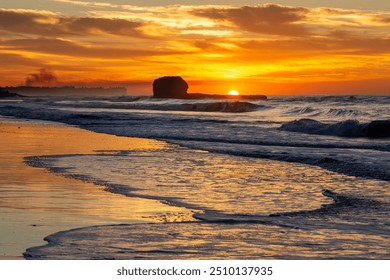 Sunrise over the water at Playa El Tunco, a popular surf beach in El Salvador. Golden light from the rising sun is seen behind the iconic rock formation and light is reflected off the sand and waves. - Powered by Shutterstock