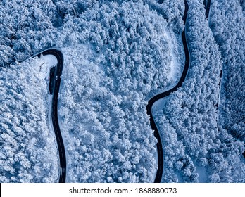 Sunrise Overhead Drone Shot Of A Mountain Alpine Road In A Snow Covered Forest And Snow Laden Pines In Early Morning In Deep Winter In Switzerland.