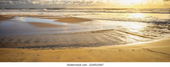 Sunrise Panorama Over A Sandy Beach On The Popular Sunshine Coast Tourist Destination In Queensland. The Glow Is Golden, The Surf Is Rough And The Tide Is On The Ebb Coming Across The Sandflats.