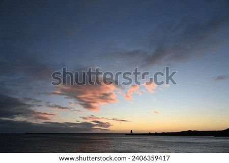 Sunrise and pink clouds at mouth of River Tyne in North East England on winter day with sun reflecting in waves.