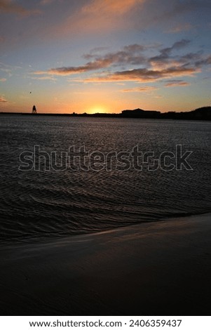 Sunrise and pink clouds at mouth of River Tyne in North East England on winter day with sun reflecting in waves.