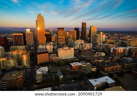 sunrise reflects off skyscraper reaching up towards the Rock Mountain background during Perfect golden hour sunrise aerial drone views above Downtown Denver Colorado USA Skyline Cityscape