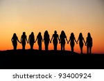 Sunrise silhouette of 10 young women walking hand in hand.