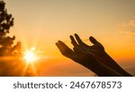 At sunrise, the silhouette of a Christian in prayer, hands lifted in worship, reflected their faith and praise, finding peace in the beauty of nature. worship, hand, praise, sunrise, pray, nature.