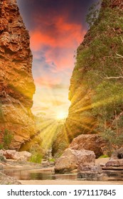 Sunrise At Simpsons Gap Gorge In The West MacDonnell Ranges In Northern Territory Of Australia With Red Steep Rocks And Sun With Bright Sunbeams Against Red Coloring Clouds