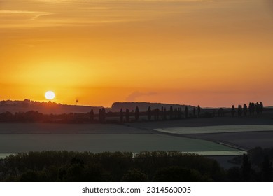 Sunrise in spring time with the silhouette of the typical Tuscan Poplar trees in a line alongside a road during the golden hour and the sun on the horizon. - Shutterstock ID 2314560005