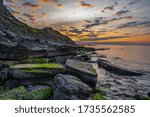 Sunrise starting over the jurassic rocks with bright green seaweed covering them and a warm orange glow in the sky with light cloud.  at Durlston Bay. Swanage, Dorset England