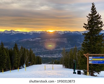 Sunrise view from the top of the ski slopes. Sun rising over the mountains warming up the ski run between the pine trees.