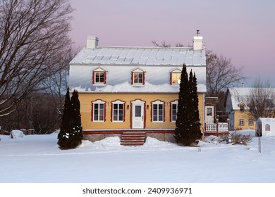 Sunrise winter view of beautiful patrimonial yellow clapboard house with silver metal Mansard roof and dormer windows, St. Pierre, Island of Orleans, Quebec - Powered by Shutterstock