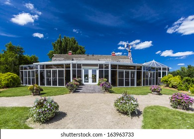 A Sunroom Attached To A Red Barn With Many Beautiful Flowers Around The Building