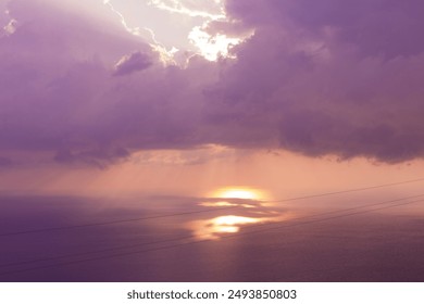 The sun's rays breaking through the violet clouds over the sea