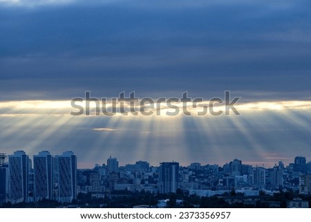 The sun's rays at dawn in the blue break through the thick clouds over the sleeping city. Shining light in a dramatic morning sky.